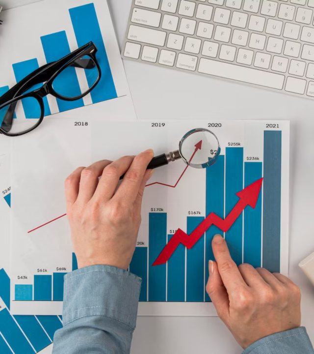 top-view-office-desk-with-growth-chart-hands-holding-magnifying-glass_23-2148780614 (1)